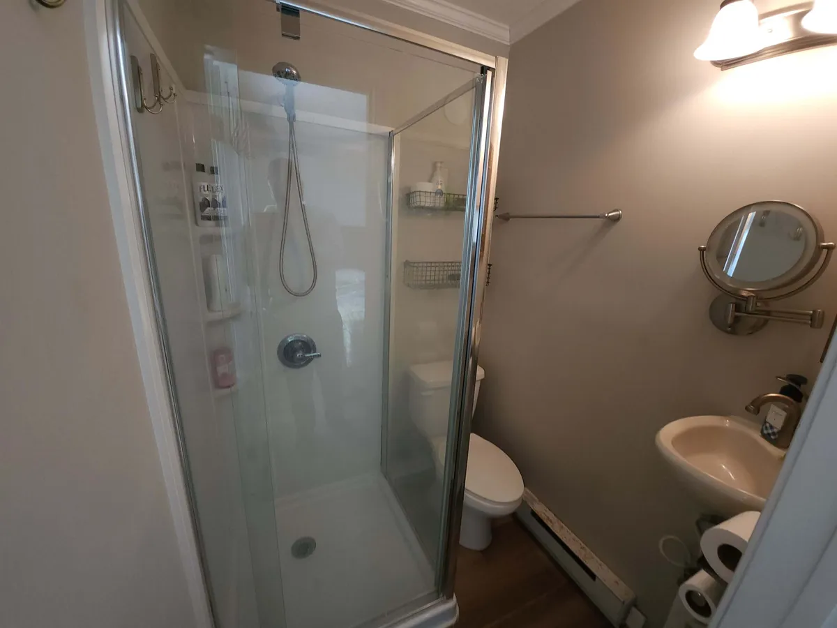 A newly remodeled full bath with a modern shower stall, sink, toilet, and minimalist mirror. The clean design emphasizes practicality and a sense of refreshment.