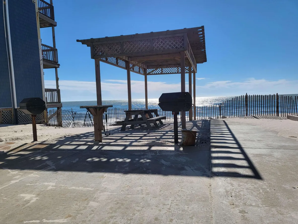 An inviting oceanfront pavilion with a picnic table, grill, and open waterfront view, perfect for social gatherings or quiet meals. The casual setup highlights relaxation and connection to nature, with the expanse of the sea as a backdrop.