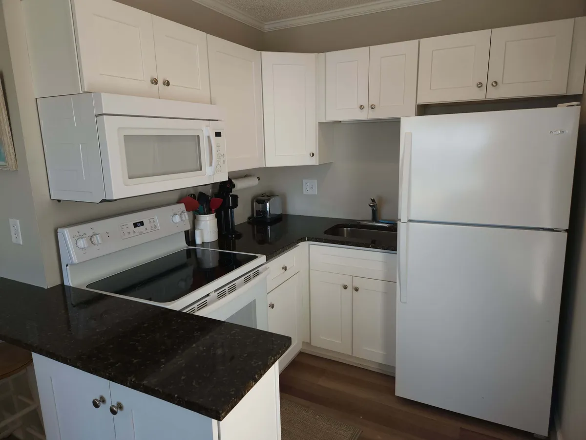 A modern kitchen with crisp white cabinetry, a striking black countertop, and contemporary appliances. The space is designed for both cooking and gathering, radiating a warm, welcoming mood.