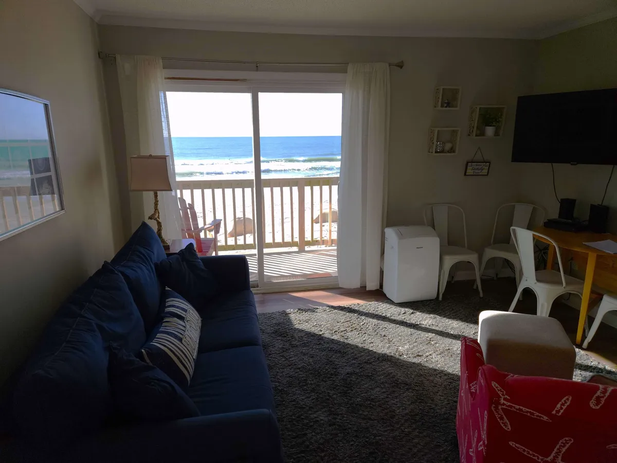 An inviting open living area with a comfortable sofa, dining table, and television, all oriented to take full advantage of sweeping ocean views. The space is bathed in natural light and exudes a casual, welcoming vibe, ideal for relaxing or gathering with family. The transition from entryway to living area is evident, guiding the eye toward the horizon.
