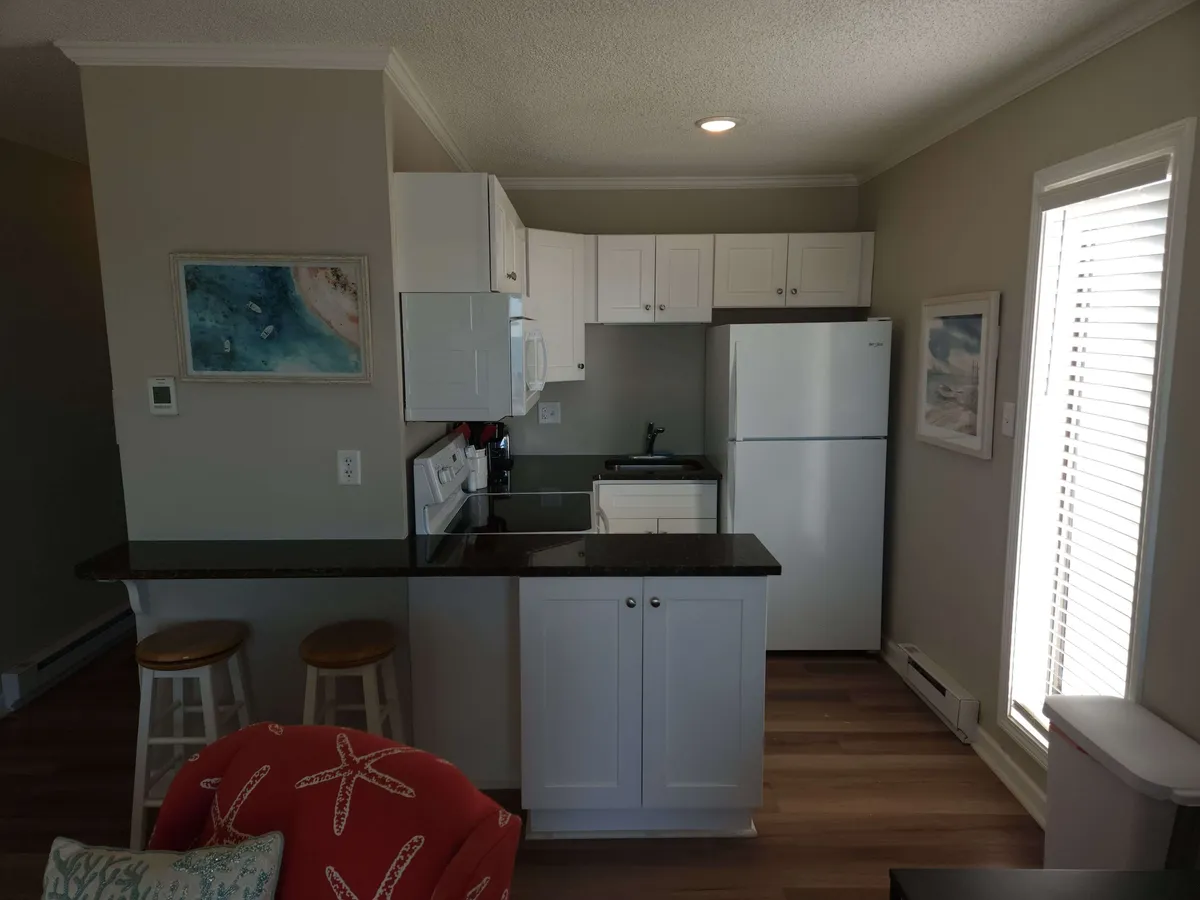 A bright, remodeled kitchen featuring a spacious island, sleek white cabinetry, stainless steel appliances, and contemporary artwork on the wall. The layout is open and inviting, perfect for cooking or socializing.