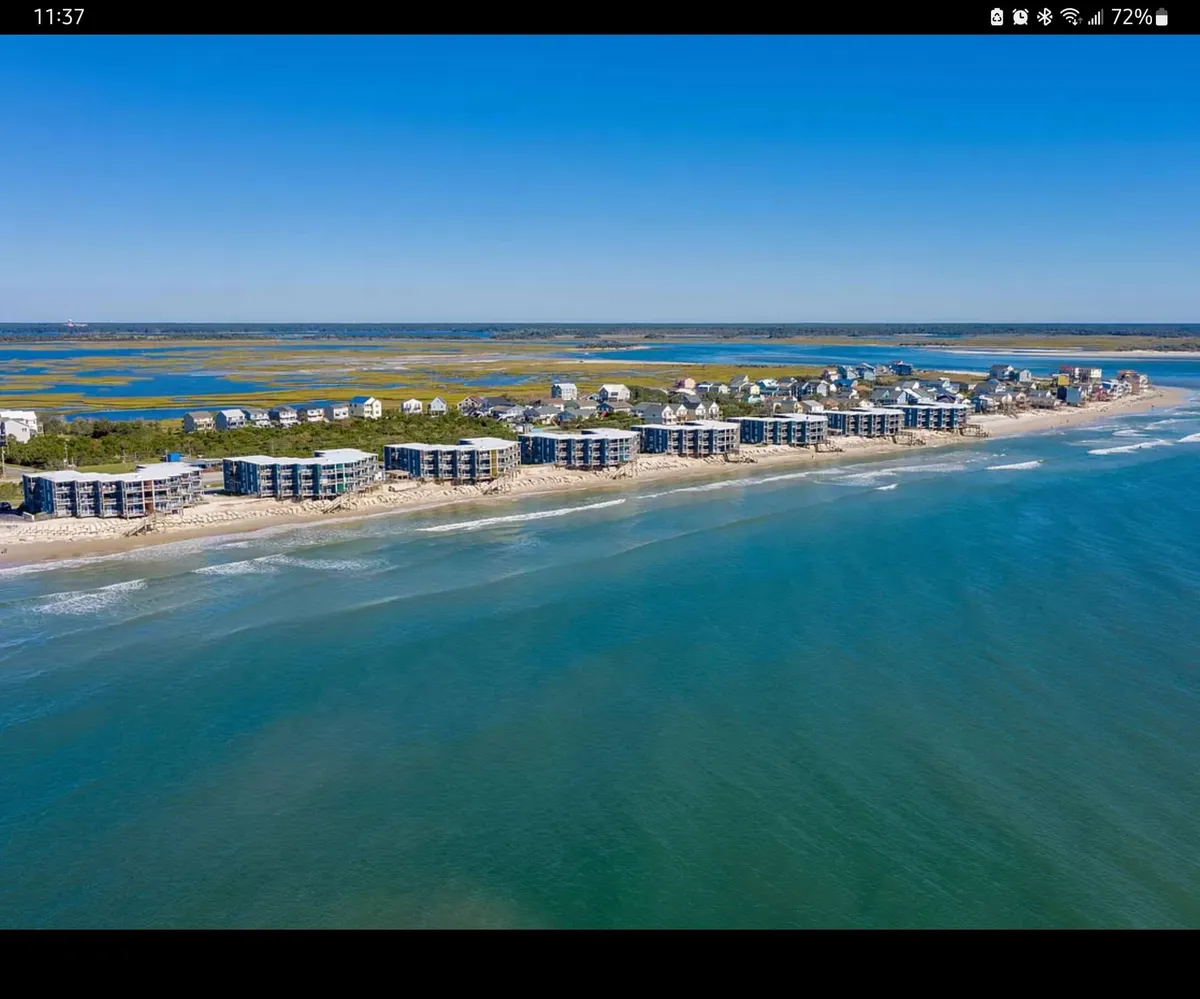 A stunning exterior view of beachfront properties overlooking the ocean, with gentle waves rolling in and distant marshes visible. The warm, golden light suggests a tranquil sunset, and the scene evokes a sense of peacefulness and relaxation. The open beach offers ample space for beachcombing, swimming, and soaking in the seaside atmosphere.
